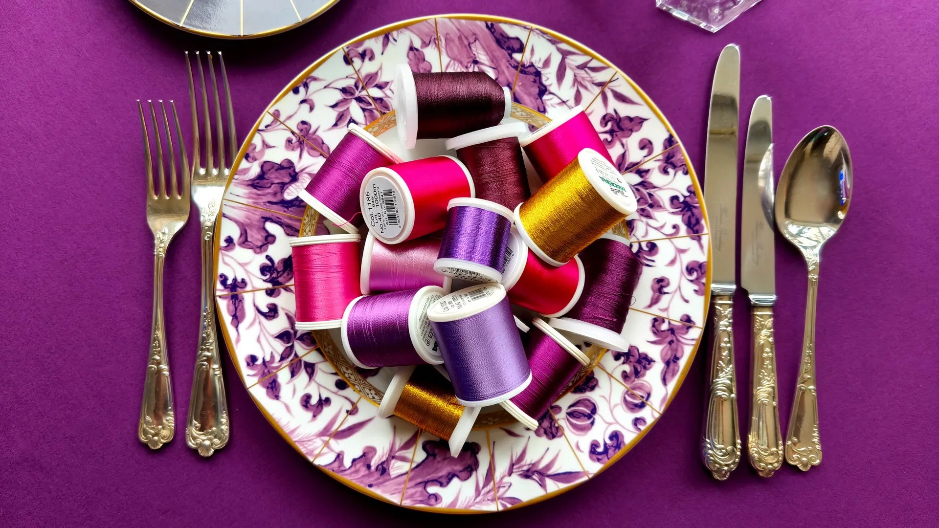 Thread spools on a decorative plate with silver cutlery on a purple background